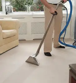 Professional carpet cleaner using a hot-water extraction wand and hose machine in a living room in Glendale, AZ.