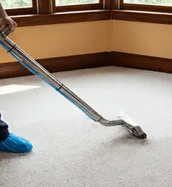 Steam carpet cleaning technician using a hot-water extraction wand on a residential carpet, wearing blue protective shoe covers Glendale, AZ.