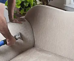 Professional upholstery cleaner deep-cleaning a fabric sofa with a handheld extraction tool and hose in Glendale, AZ.
